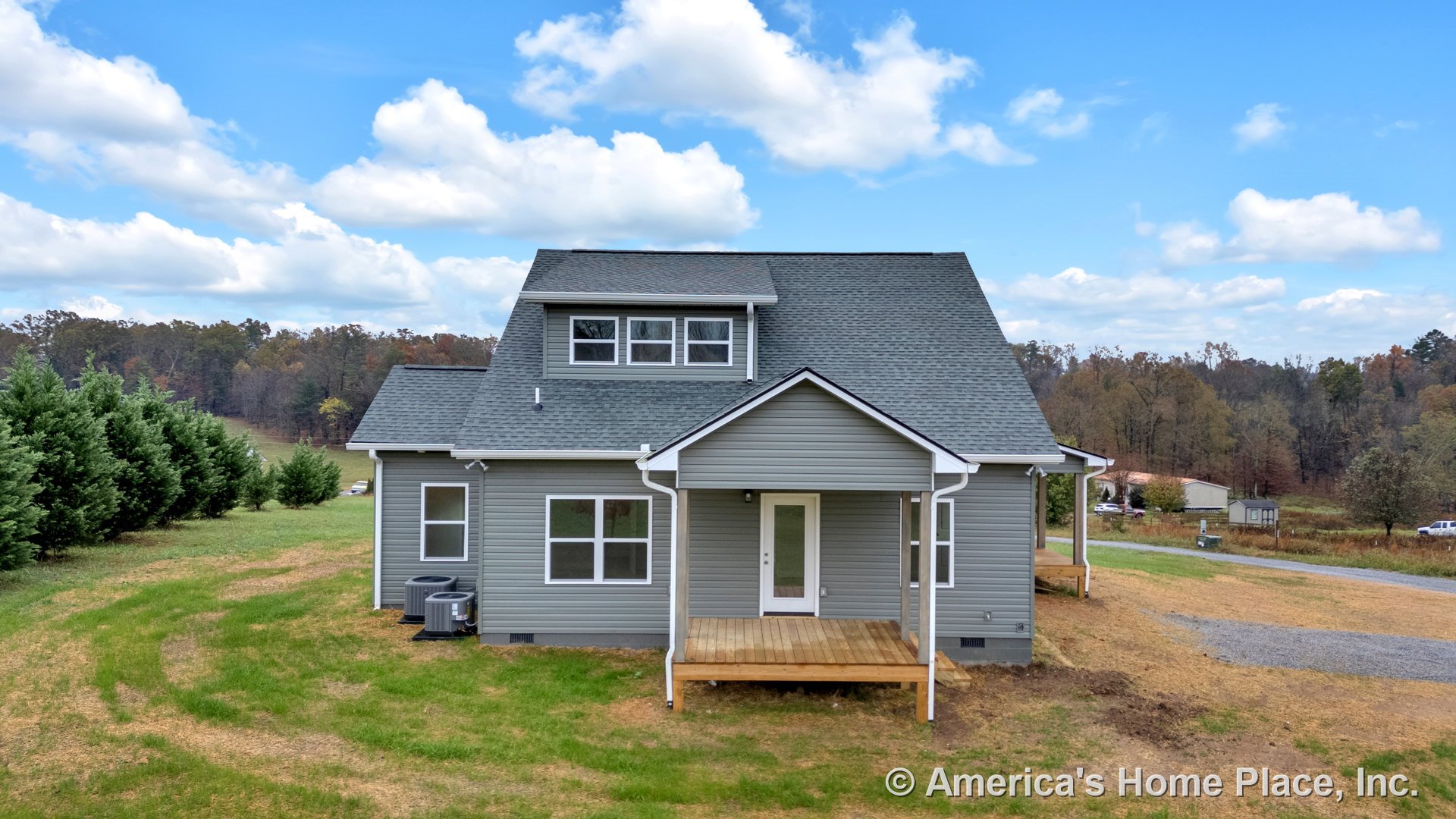 Gray vinyl siding with white trim and gutters, covered front porch, multiple double-hung windows, architectural shingle roof, exterior HVAC units, and entry door in a rural new