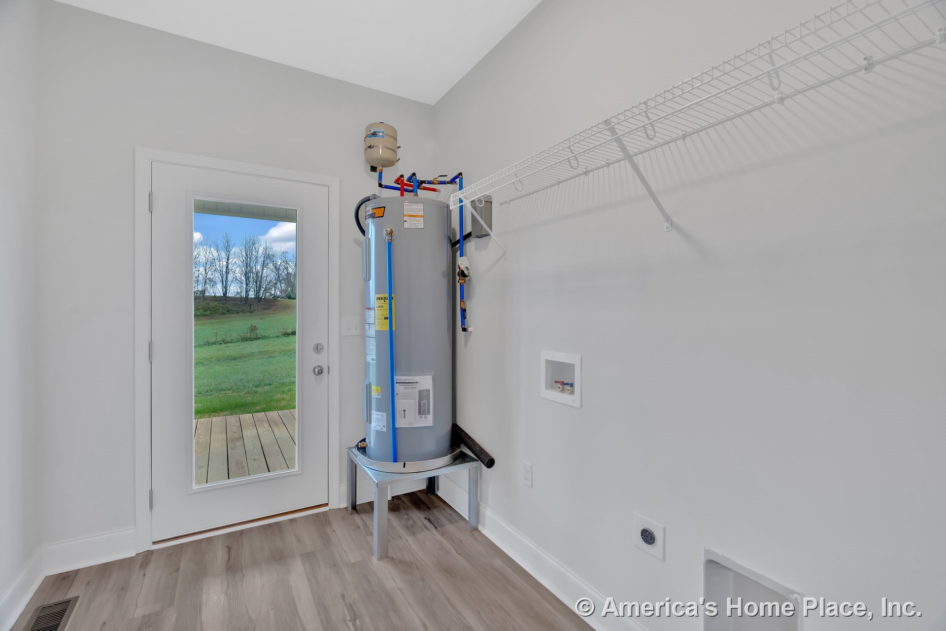Laundry room with mounted water heater, utility hookups, white wire shelving, glass exterior door to backyard, light wood-look vinyl flooring, white trim and baseboards, neutral