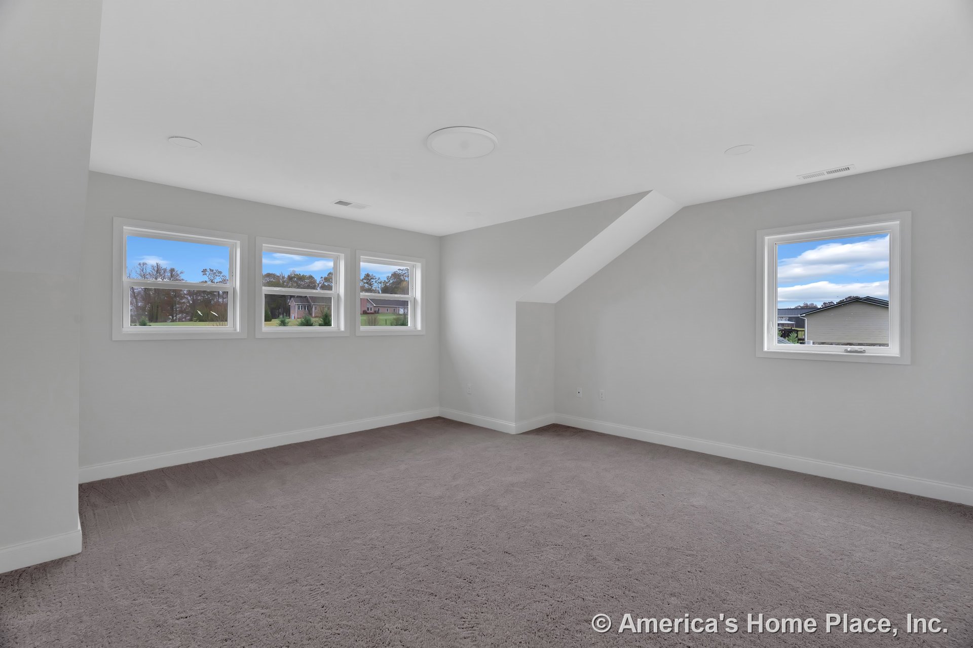 Upstairs room with four rectangular windows, light gray carpet flooring, white baseboards, angled ceiling detail, neutral wall paint, and recessed ceiling fixture.