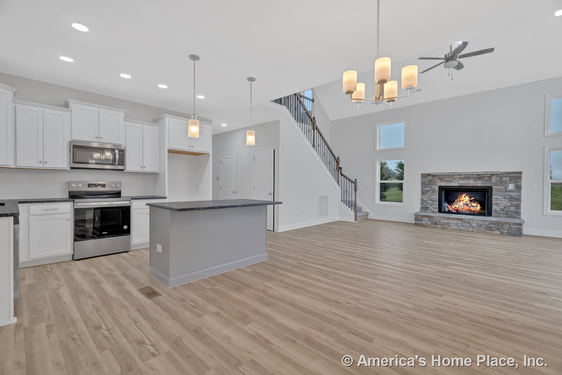 Open concept kitchen and living area with white shaker cabinets, stainless steel appliances, stone surround fireplace, wood-look vinyl plank flooring, pendant and chandelier