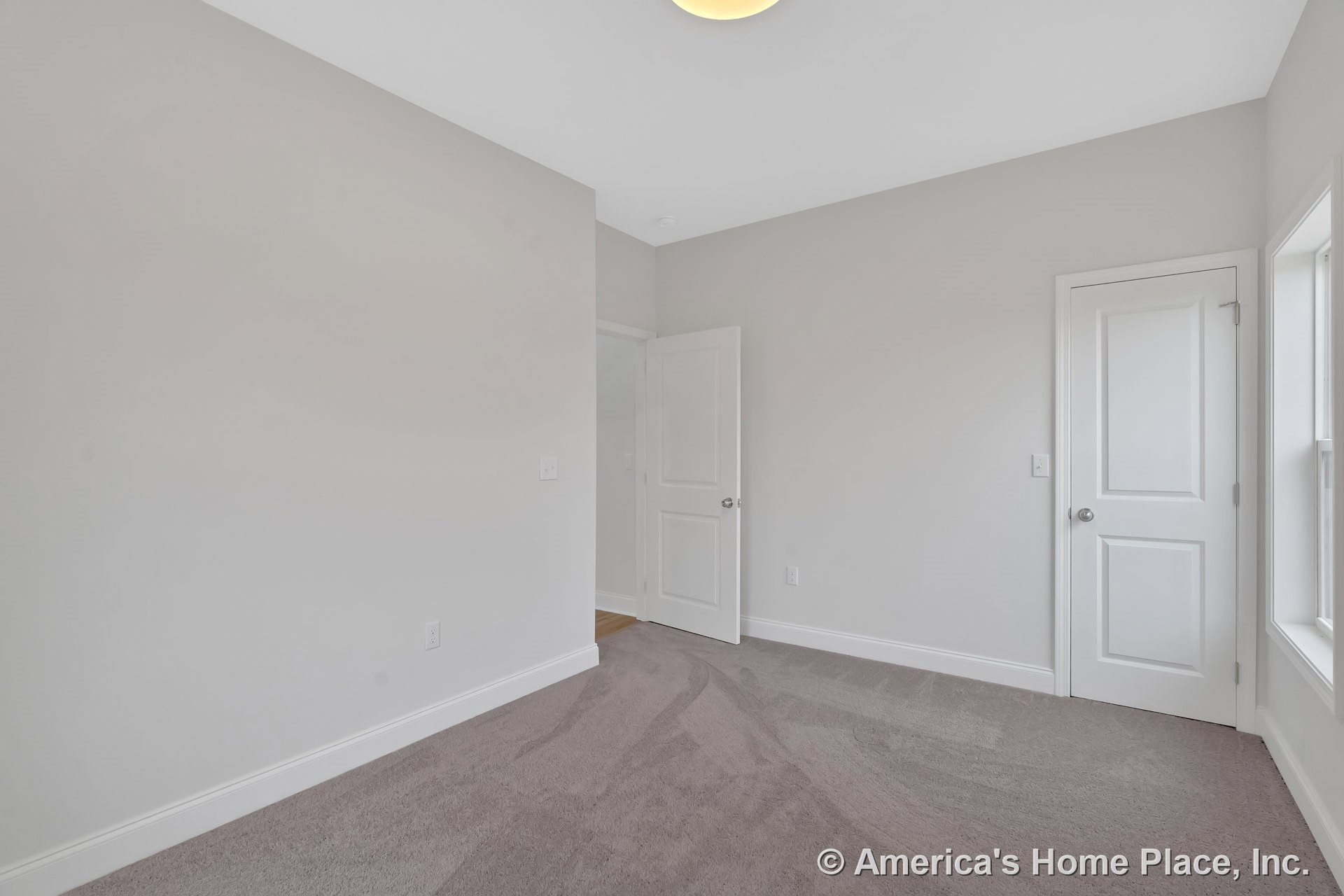 Bedroom with light gray carpet flooring, white baseboards and trim, two white paneled doors, large window allowing natural light, neutral wall color, and flush-mounted ceiling