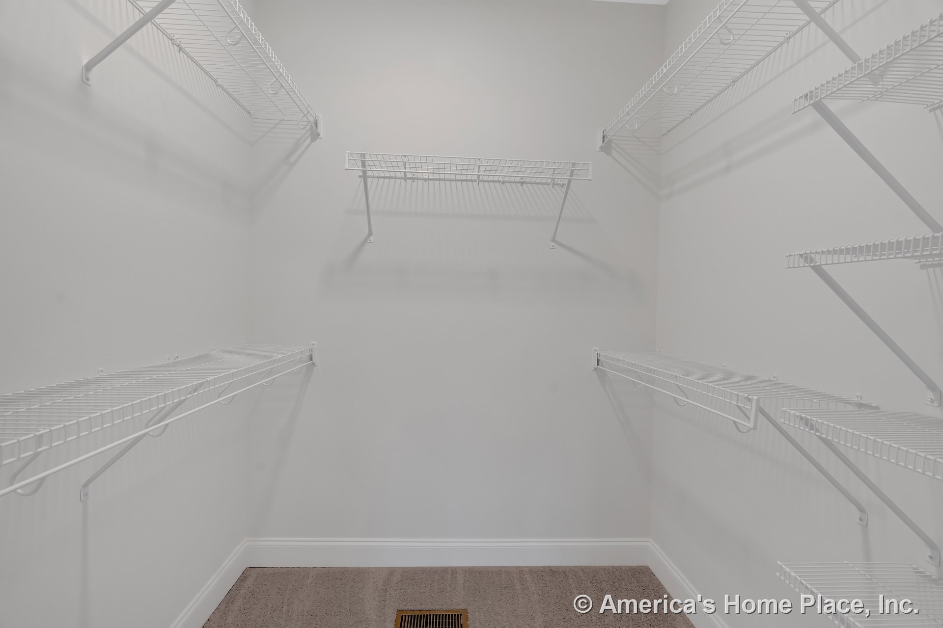 Walk-in closet with multiple white wire shelving units, neutral carpet flooring, light gray walls, white baseboard trim, and floor vent.