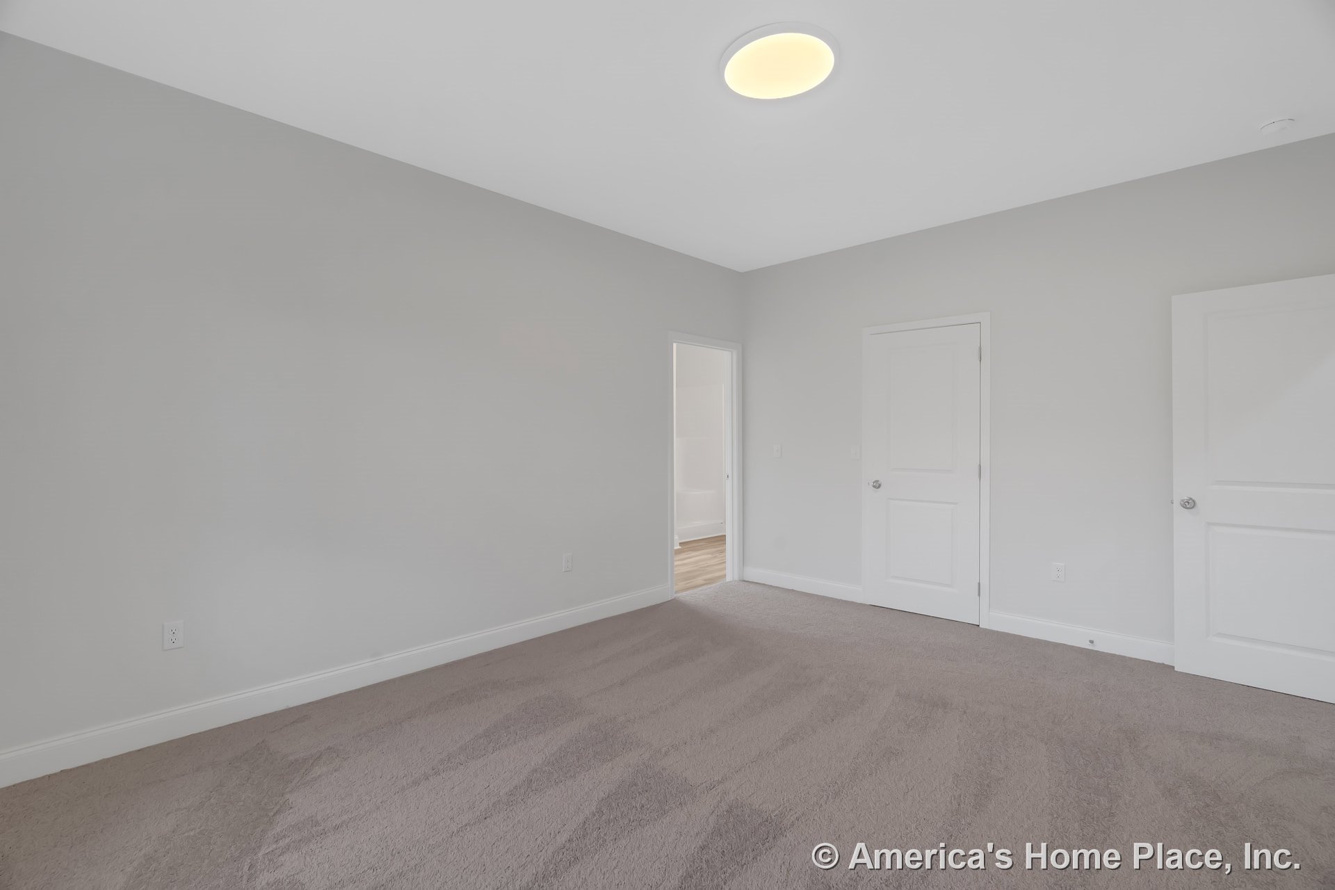 Bedroom with light gray carpet, white baseboards, neutral painted walls, flush ceiling light, and two white paneled doors including a doorway to an adjacent room.