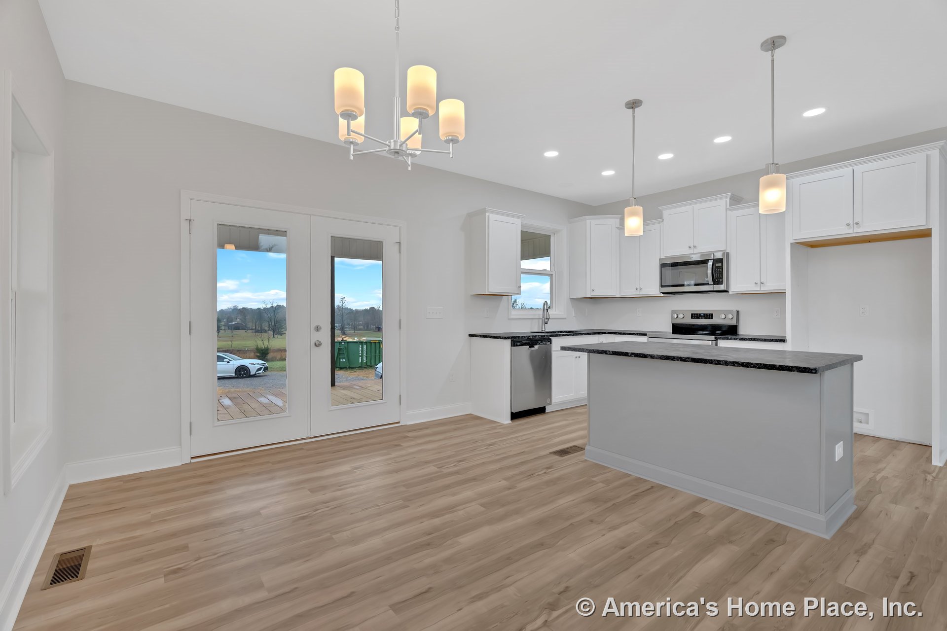 White kitchen cabinetry with granite island countertop, stainless steel oven and microwave, pendant and chandelier lighting fixtures, light wood flooring, adjacent dining area