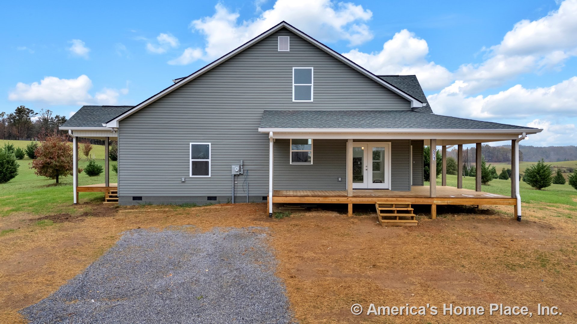 Covered front porch with wood deck steps, gray vinyl siding, double front doors with white trim, gabled roof, and multiple windows in a rural setting.