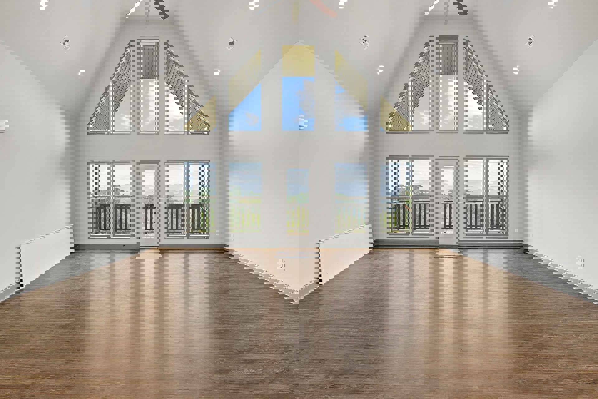 Spacious living area with wood flooring, ceiling fan, multiple windows, white door featuring a central cutout, doors opening to a balcony with mountain and valley views under a
