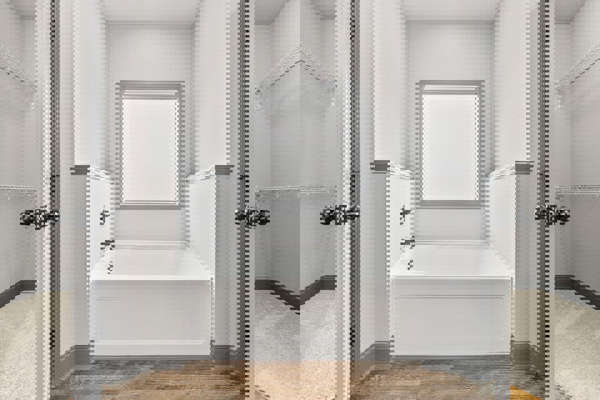 Freestanding white bathtub with chrome floor-mounted faucet, white tile walls, minimalist decor, and framed artwork above tub in modern bathroom