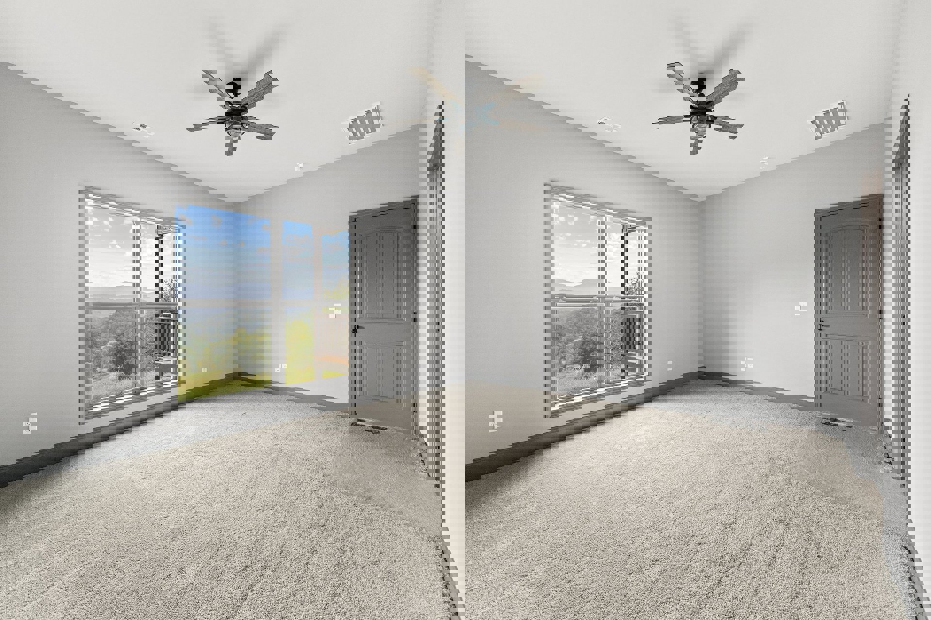 Carpeted room with white door featuring black knob, ceiling fan with light, large window overlooking valley and mountains, and wooden deck railing visible outside.