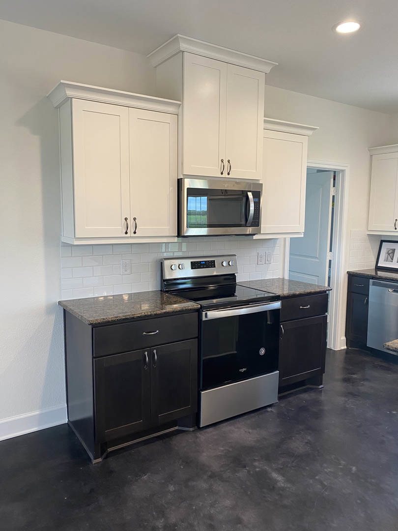 Modern kitchen featuring black lower cabinets, white upper cabinets, marble countertop, stainless steel microwave and oven, black and silver stove, light wood flooring, and framed