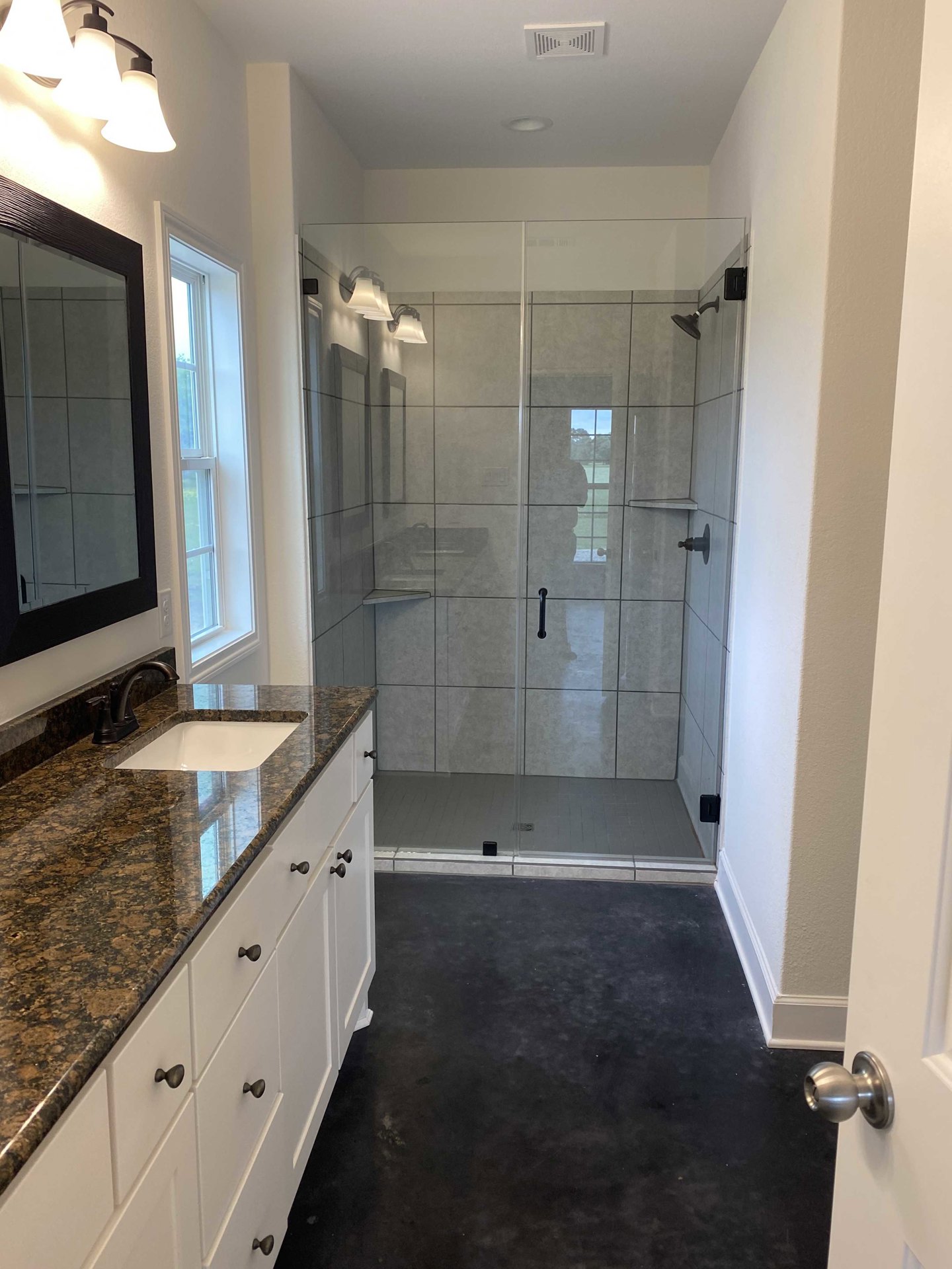 Bathroom featuring a glass shower enclosure, white countertop with black-handled cabinets, modern three-light fixture, and a close-up of a freestanding bathtub; tile flooring and