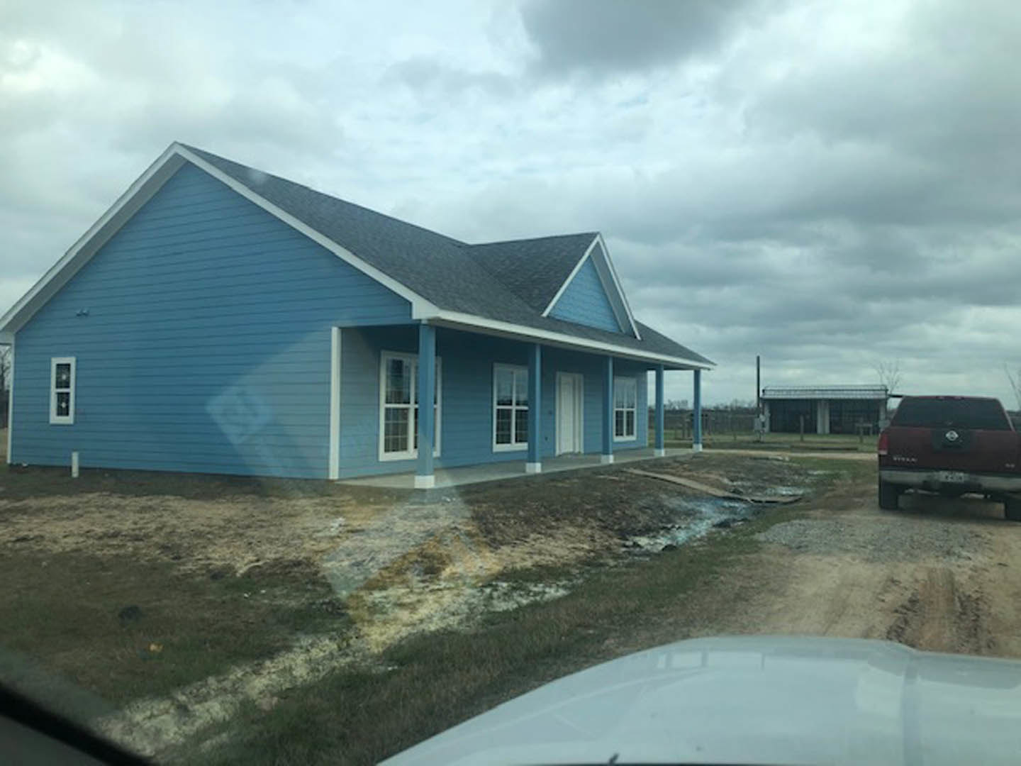 Blue house with white roof and trim, red truck parked on street, white-framed windows, cloudy sky overhead