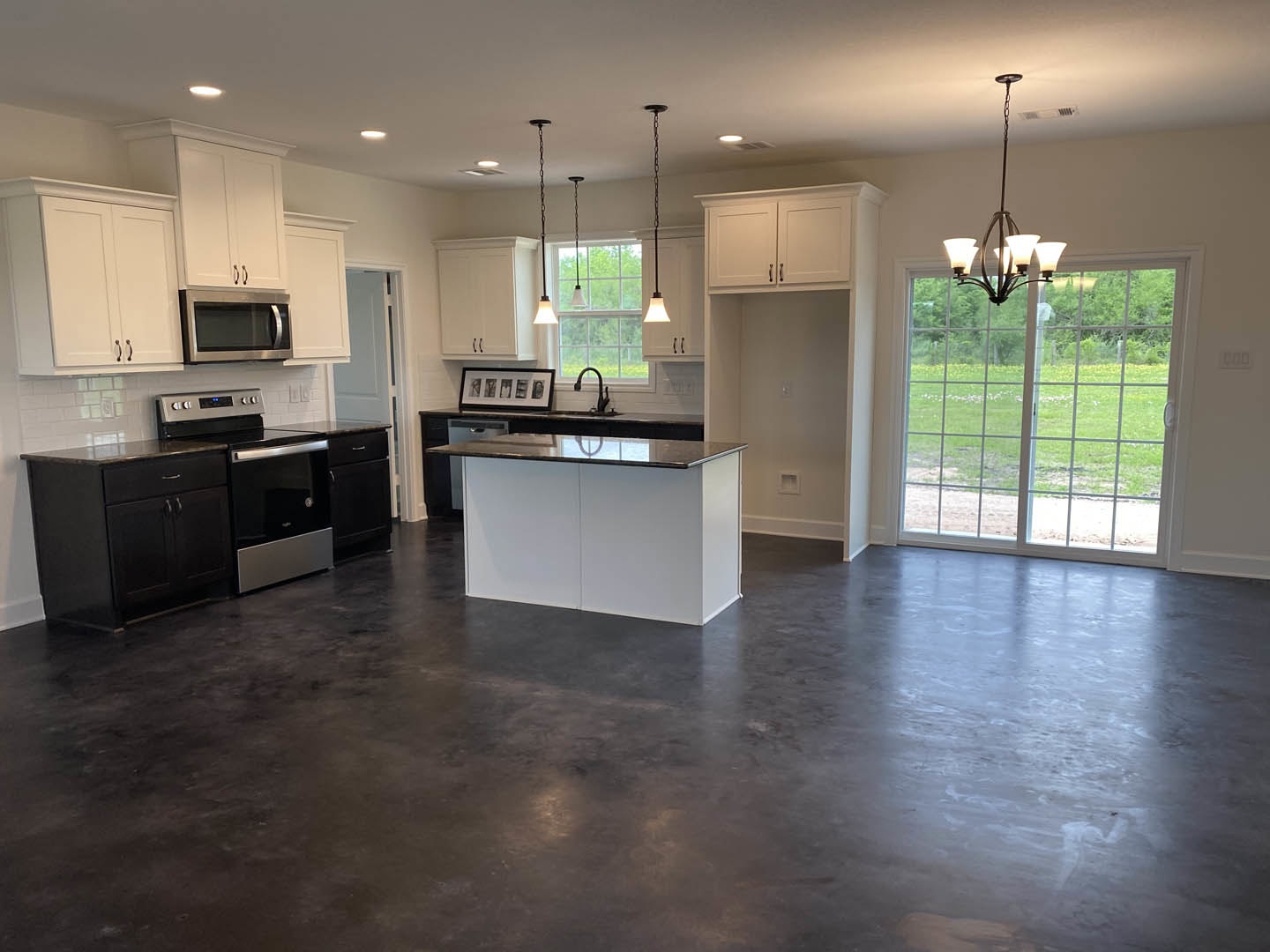 Spacious kitchen featuring a large island with contrasting white and black countertops, dark flooring, glass door, modern cabinetry, built-in microwave, chandelier near window, and