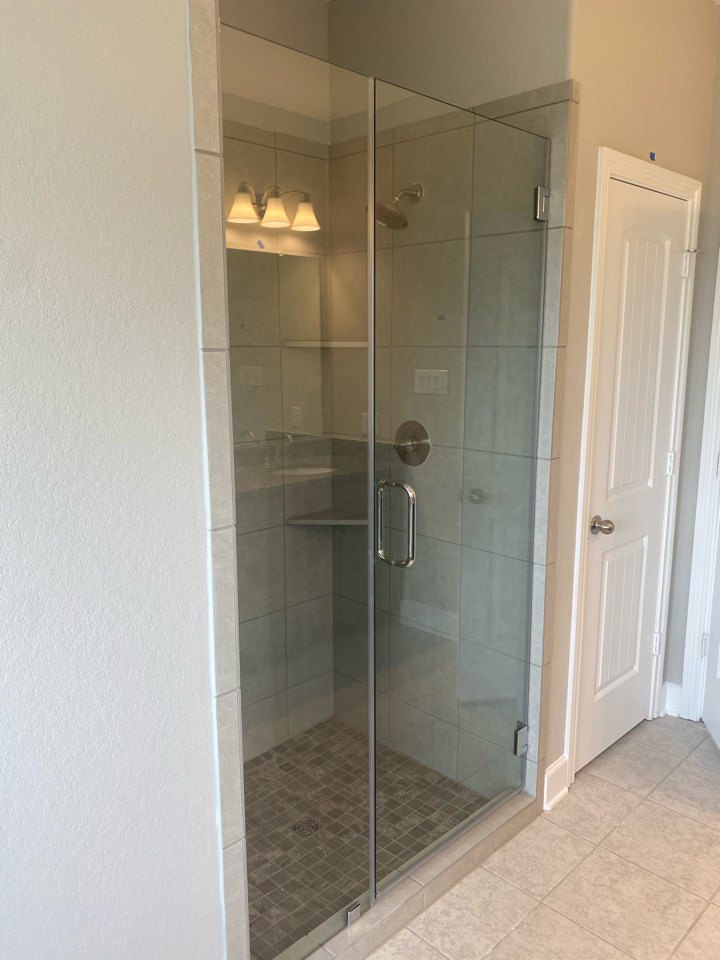 Frameless glass shower enclosure with chrome fixtures, white tile walls, adjacent vanity sink, and wall-mounted lighting in a modern bathroom