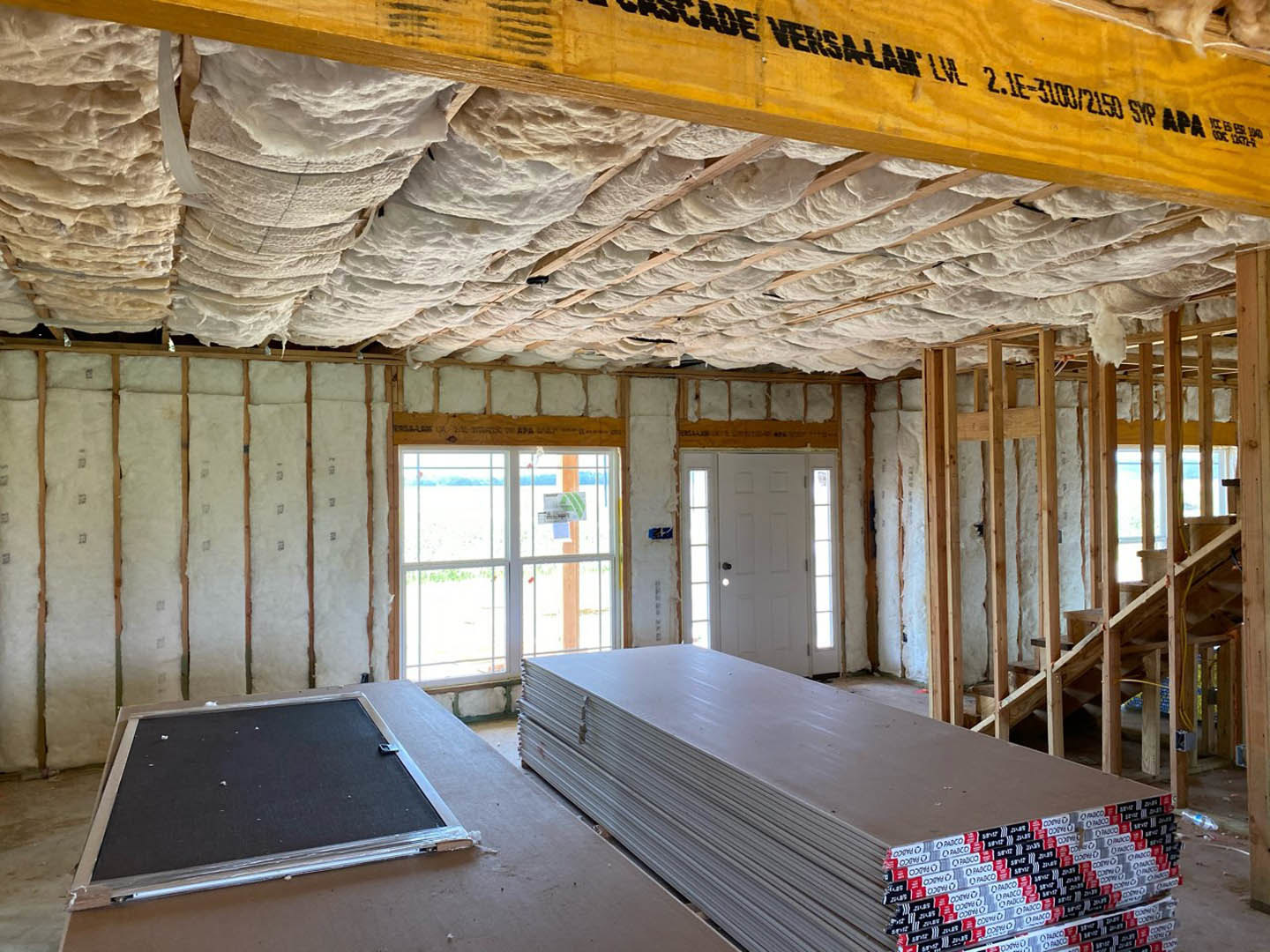 Room with stacked wood panels and planks, black board with silver frame, boxes with printed text, window displaying a sign, white ceiling material