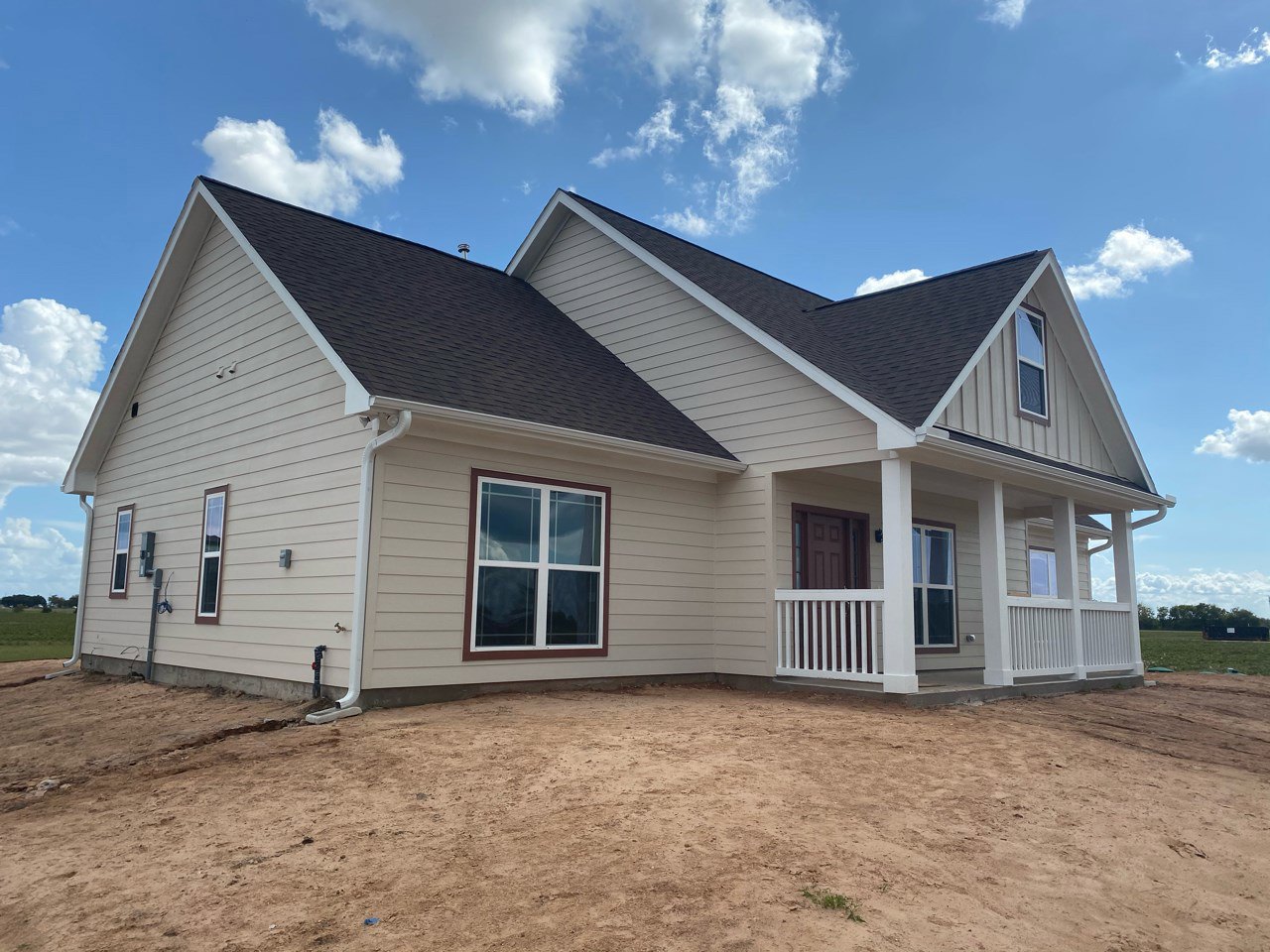 White house with white framed windows and railing, set against a dirt hill, blue sky with scattered clouds above, exposed ground in front of the building.