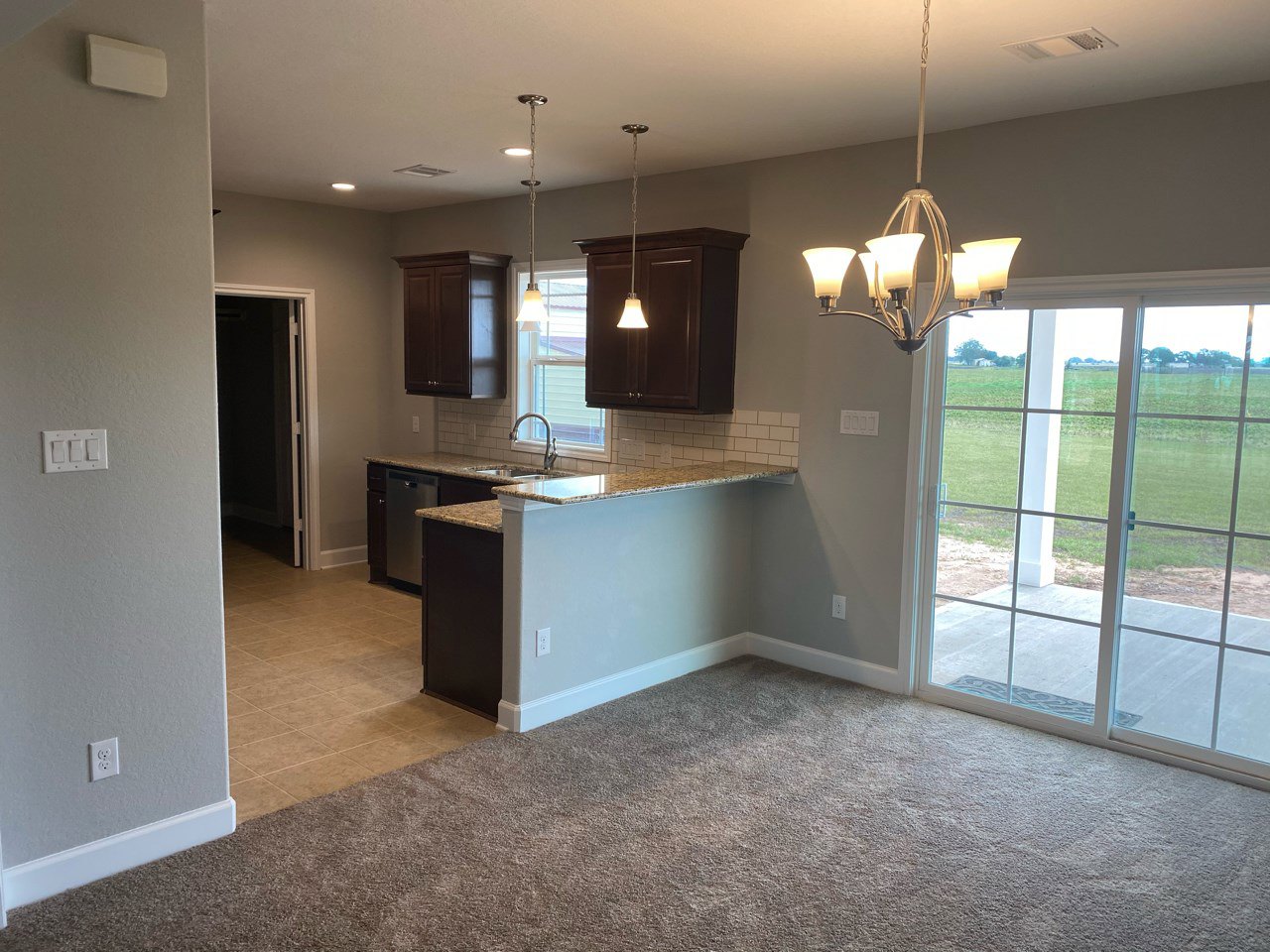 Open kitchen and dining area featuring wood cabinetry, stone countertops, pendant chandelier, and a glass door overlooking a green field