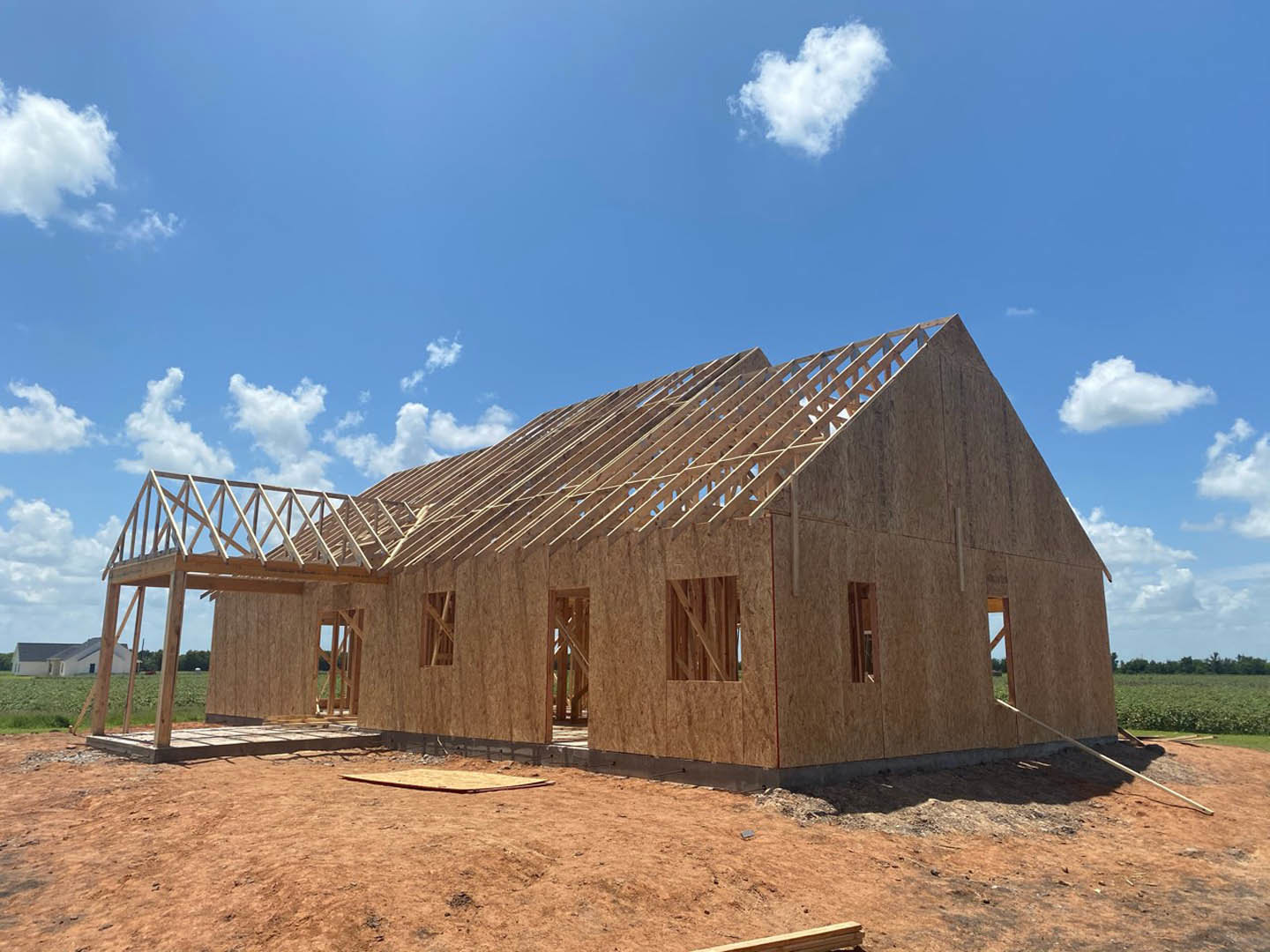 Wood-framed house under construction with completed roof, exposed beams, and heart-shaped cloud in blue sky above