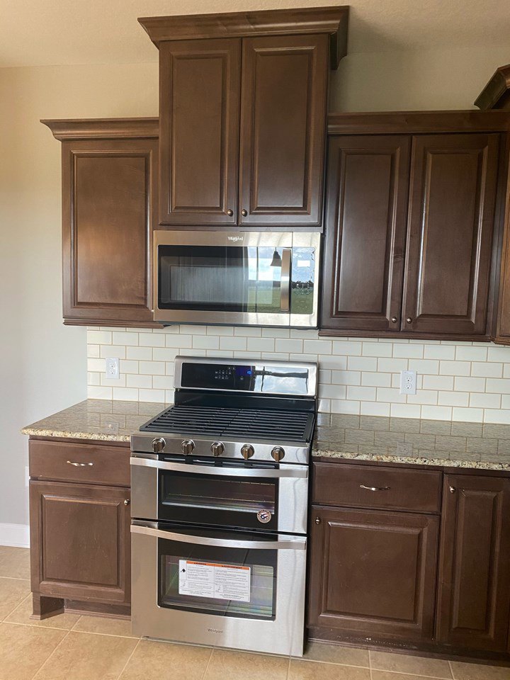 Modern kitchen featuring stainless steel stove, built-in microwave above, white cabinetry, stone countertops, and tile backsplash