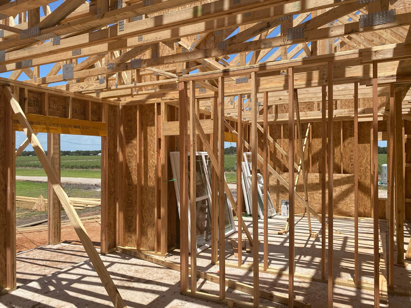 Wooden house frame under construction with exposed beams, planks, and window opening on dirt ground