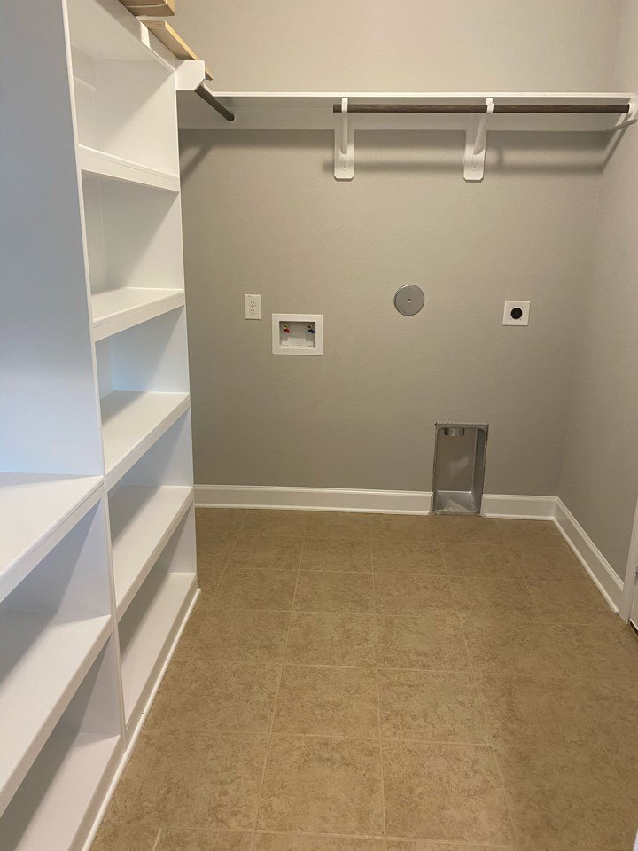 Bathroom with gray painted wall, white built-in shelves, brown tile flooring, white baseboard trim, silver rectangular fixture, and white cabinetry.
