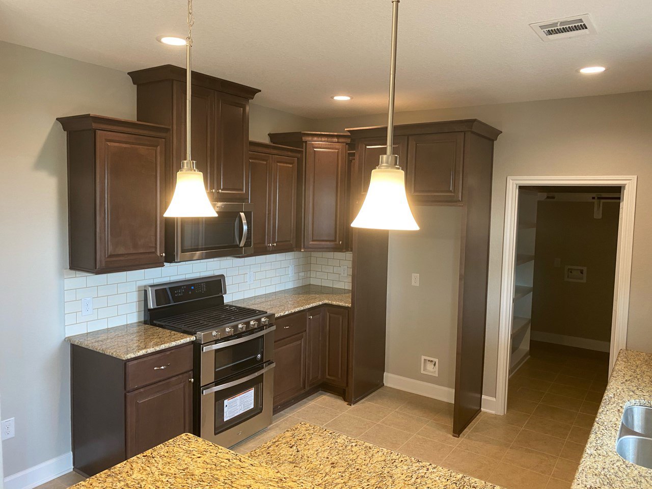 Dark wood kitchen cabinets, marble countertop, stainless steel stove and oven, built-in microwave, pendant light fixture, neutral walls, modern finishes