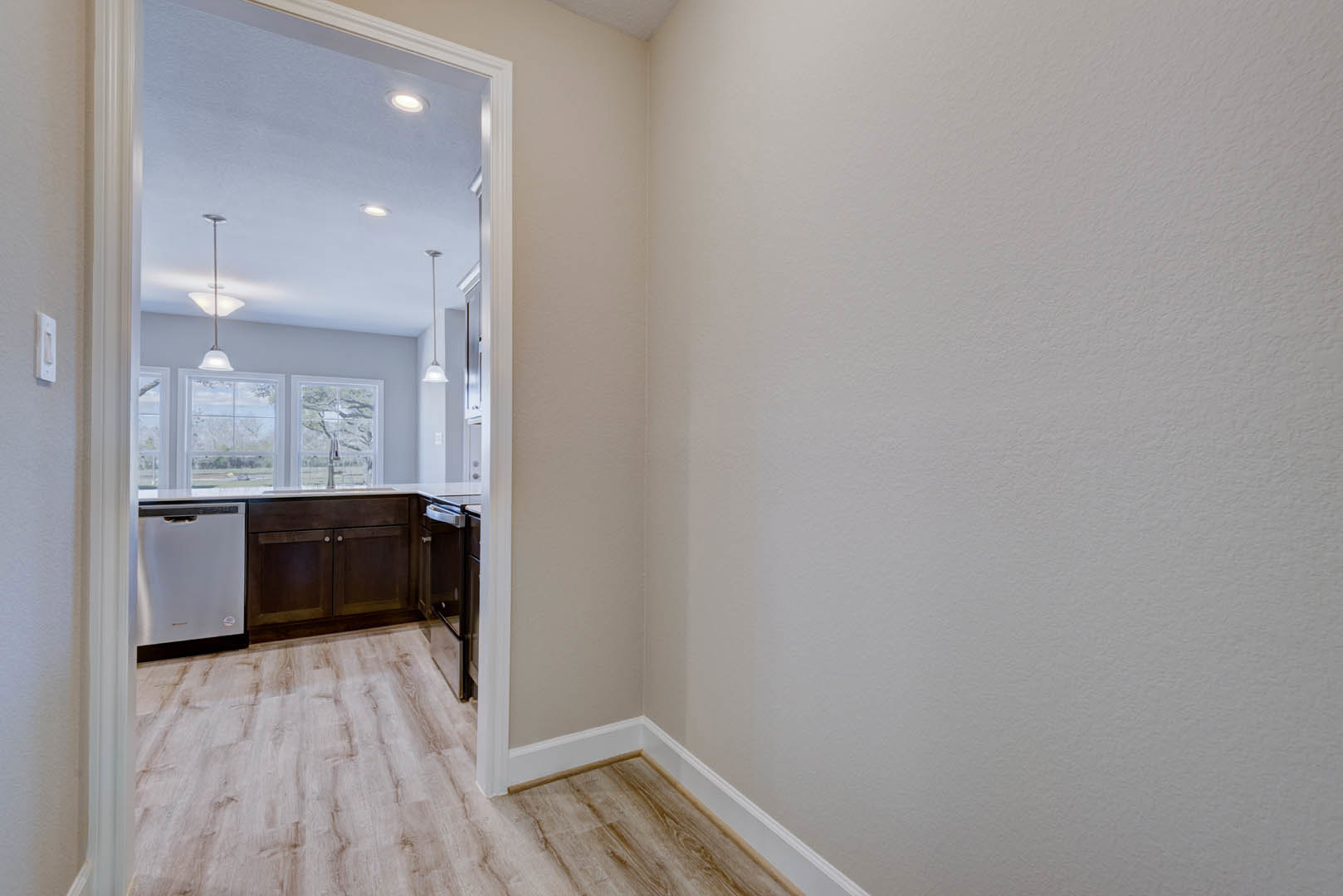 Open white door leading to a room with light laminate flooring, white plaster walls, silver refrigerator, white-framed window, and modern cabinet.