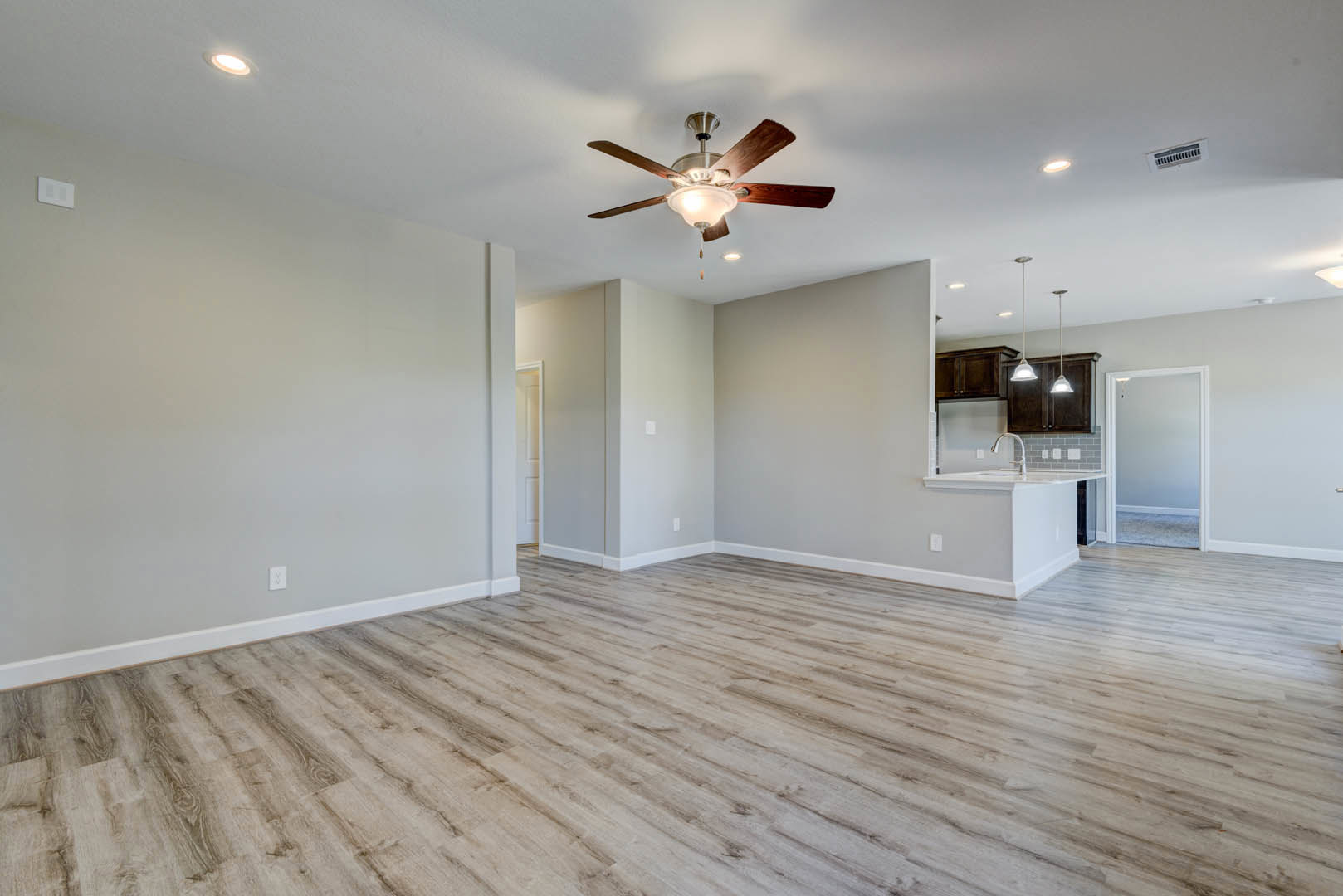 Open kitchen with white cabinetry, wood laminate flooring, ceiling fan with light fixture, and adjacent doorway visible against plaster walls.