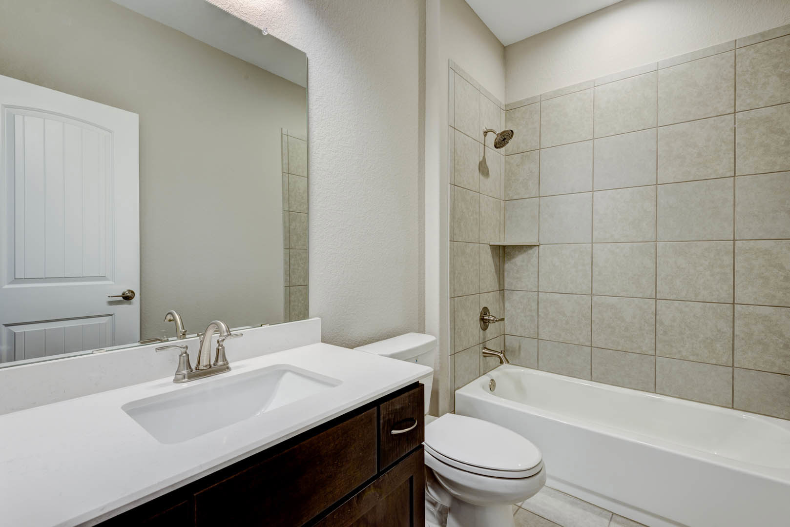 Modern bathroom featuring a freestanding white bathtub, sleek sink with chrome faucet, white door with silver handle, and toilet with closed lid; light tile flooring and neutral