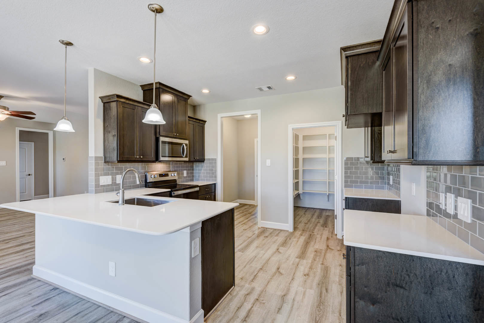 Kitchen with wood flooring, white countertops, white cabinetry, stainless steel sink on a central island, built-in microwave, recessed ceiling light, and open closet shelving