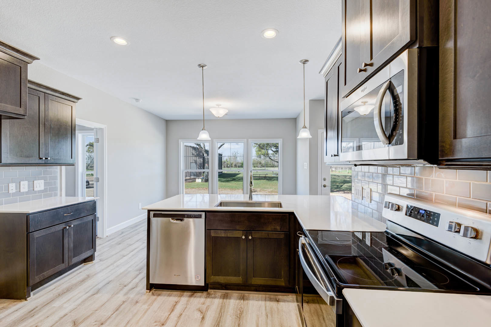 Kitchen with light wood flooring, white walls, white cabinetry, stainless steel appliances including a microwave and stove, silver water heater, and a window overlooking a green