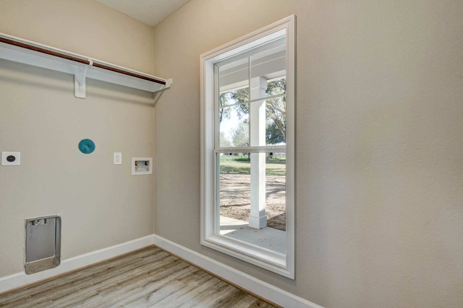 Sunlit room featuring a large window with white trim, wood plank flooring, and white baseboards against smooth plaster walls