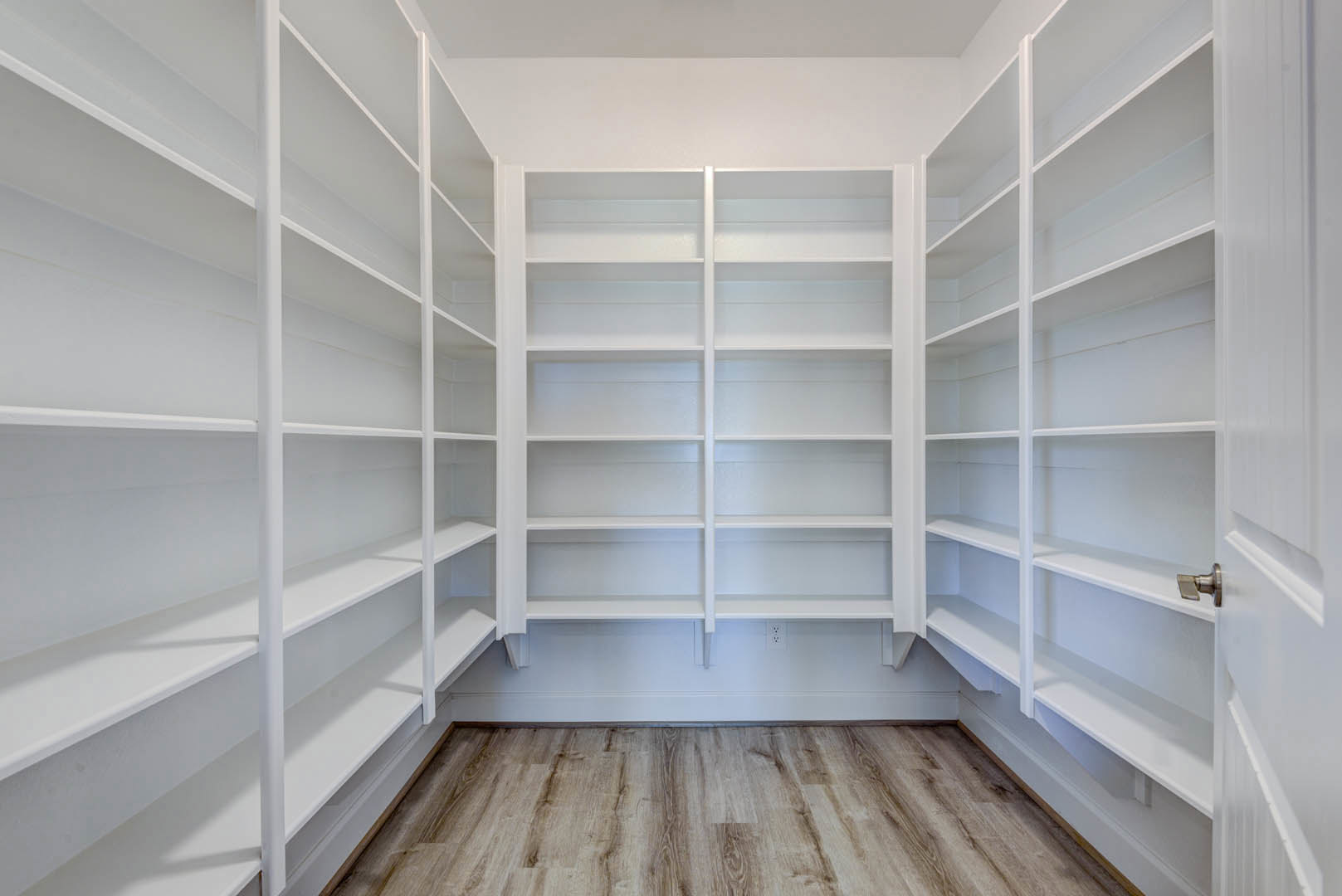 White built-in shelves along a plaster wall, empty and neatly arranged, with light wood flooring and a window providing natural light in a modern room.
