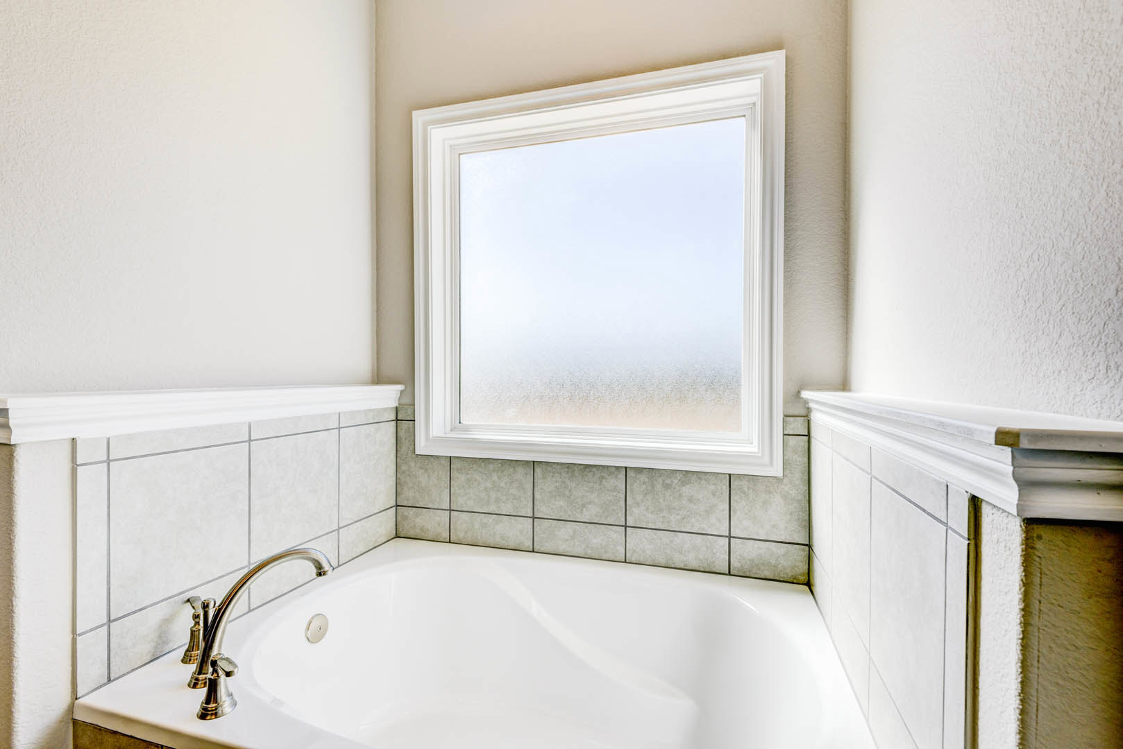 White freestanding bathtub beneath frosted glass window, chrome faucet, white tiled walls, minimalist shelf above tub