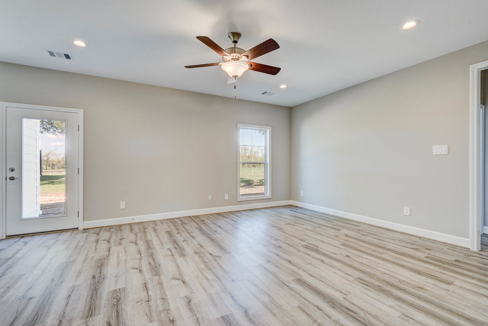 Ceiling fan with integrated light fixture, hardwood flooring, plaster walls, glass-paneled door, large window overlooking open field