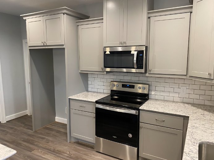 White shaker cabinets, black stove with matching oven, stainless steel microwave above, quartz countertops, undermount sink with chrome faucet