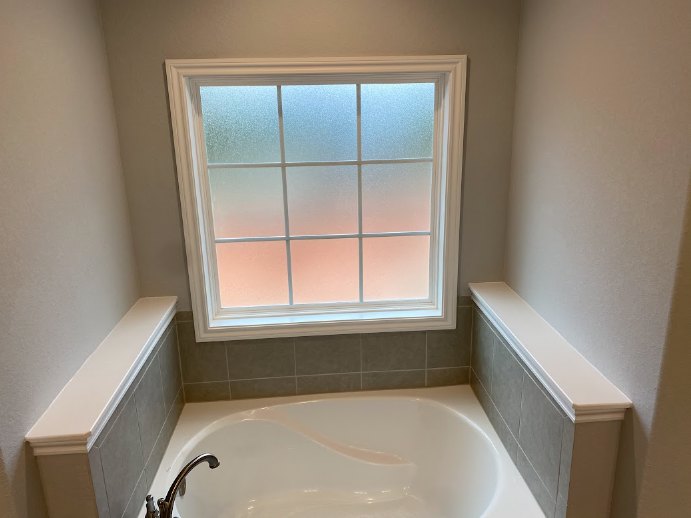 White freestanding bathtub beneath a large window, surrounded by light tile walls and chrome fixtures in a modern bathroom