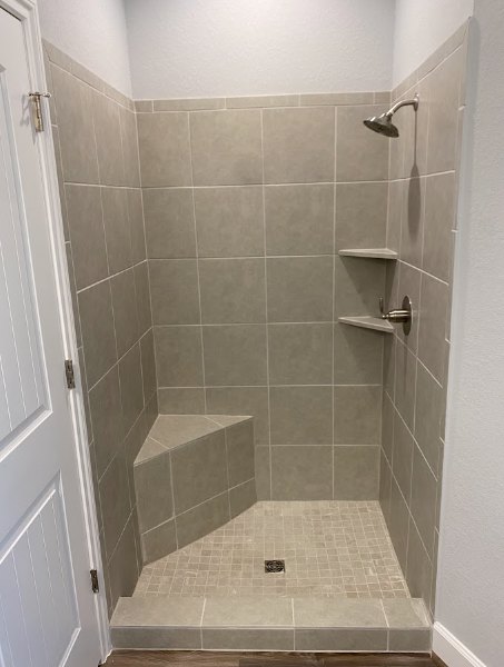 Walk-in shower with chrome shower head, marble tile walls, and light-colored tile flooring