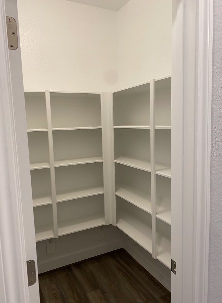 White built-in shelves inside a closet with dark wood flooring and white baseboards, surrounded by white walls and door frame.