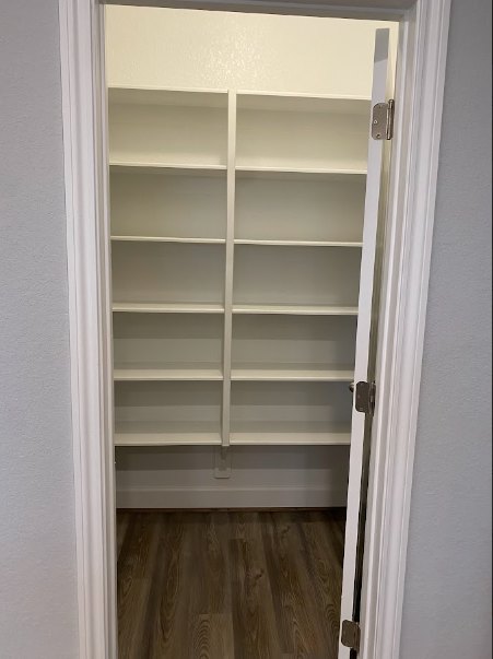 Walk-in closet with white built-in shelves, hardwood floor, and natural light from a window