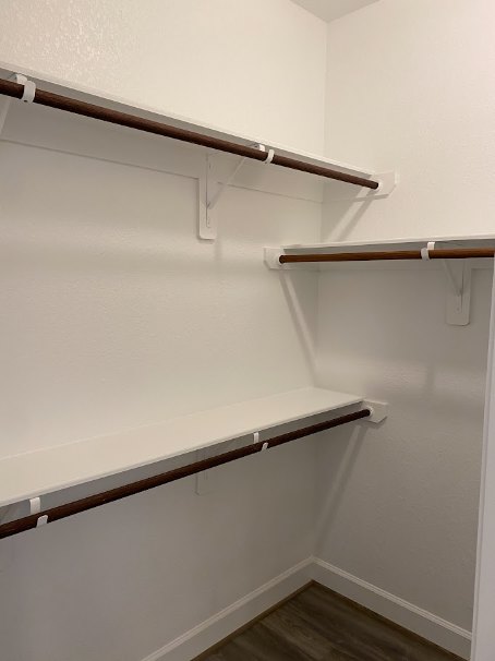 White closet with built-in shelves, wood flooring with white trim, white door featuring a horizontal bar, and wooden shelf with a brown handle.
