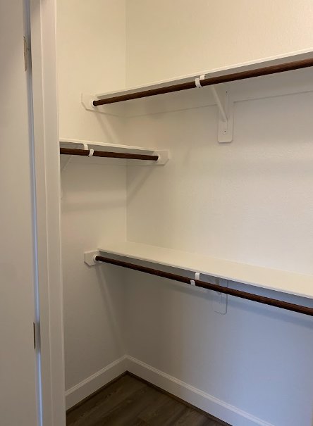 Walk-in closet with white shelves, metal hanging rods, wood flooring, and a white door
