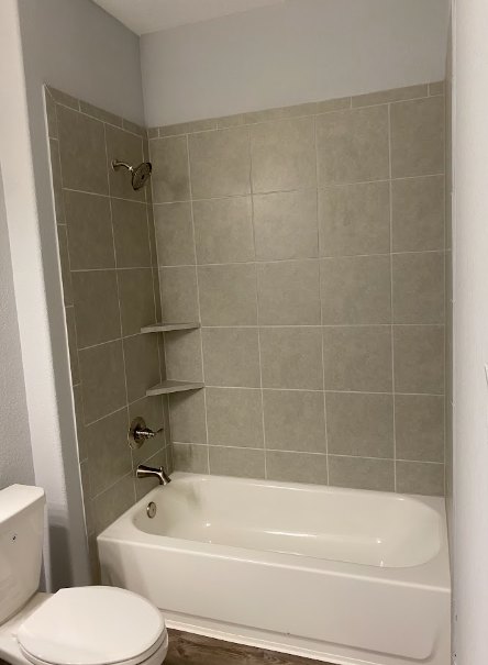 White freestanding bathtub next to a tiled wall with built-in corner shelves, adjacent to a modern toilet on a light tile floor