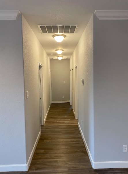 Hallway with white walls, white trim, wood flooring, ceiling light fixture, and a light switch on the wall