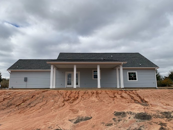 Two-story house with white pillars and glass-paneled door, front porch overlooking a dirt hill, cloudy sky above