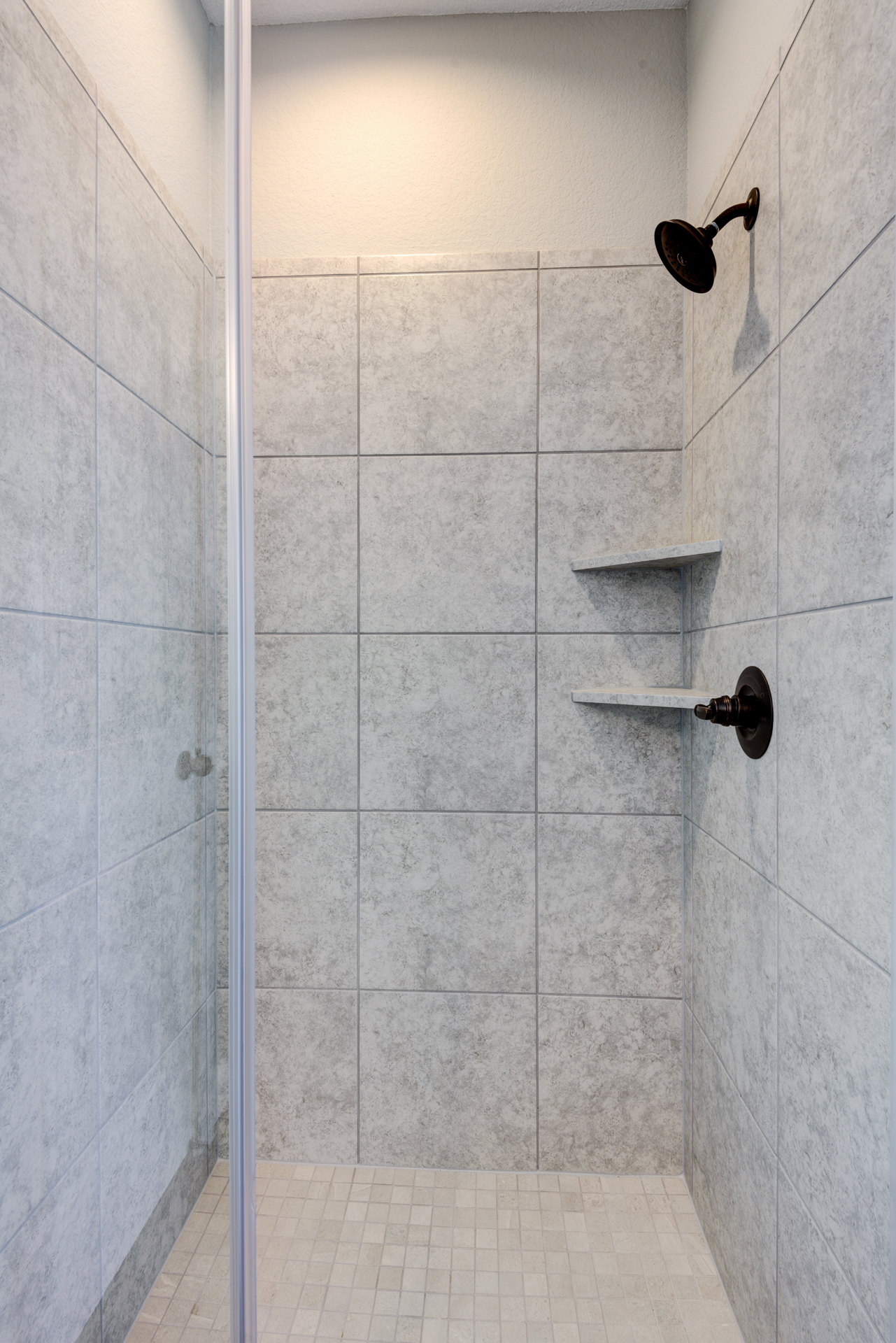 Tile shower with chrome shower head, built-in shelf, and textured tile wall and floor