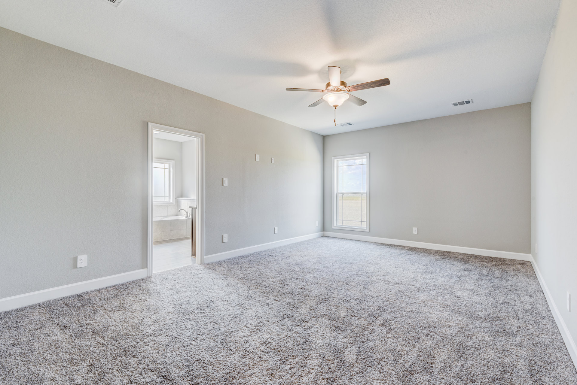 Carpeted room with white walls, ceiling fan with light fixture, large window overlooking grassy field, natural light illuminating neutral finishes