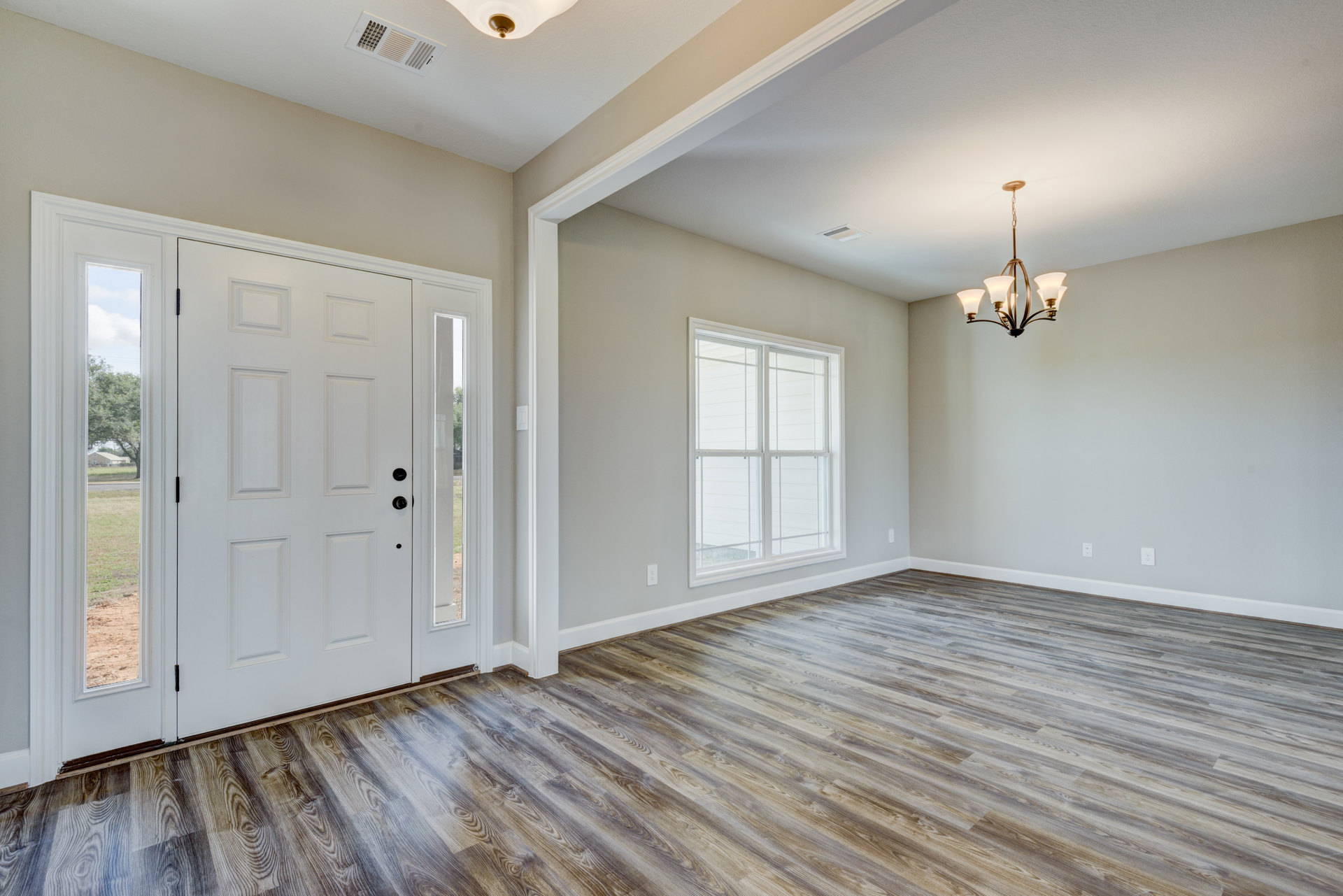 Wood floor room featuring a white door with glass panes, white-trimmed window, and chandelier hanging from a white ceiling with crown molding.
