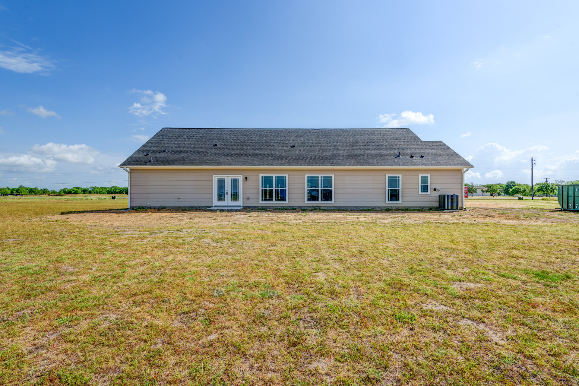 Two-story farmhouse with white-framed windows, glass-paneled double doors, and expansive green lawn under partly cloudy sky