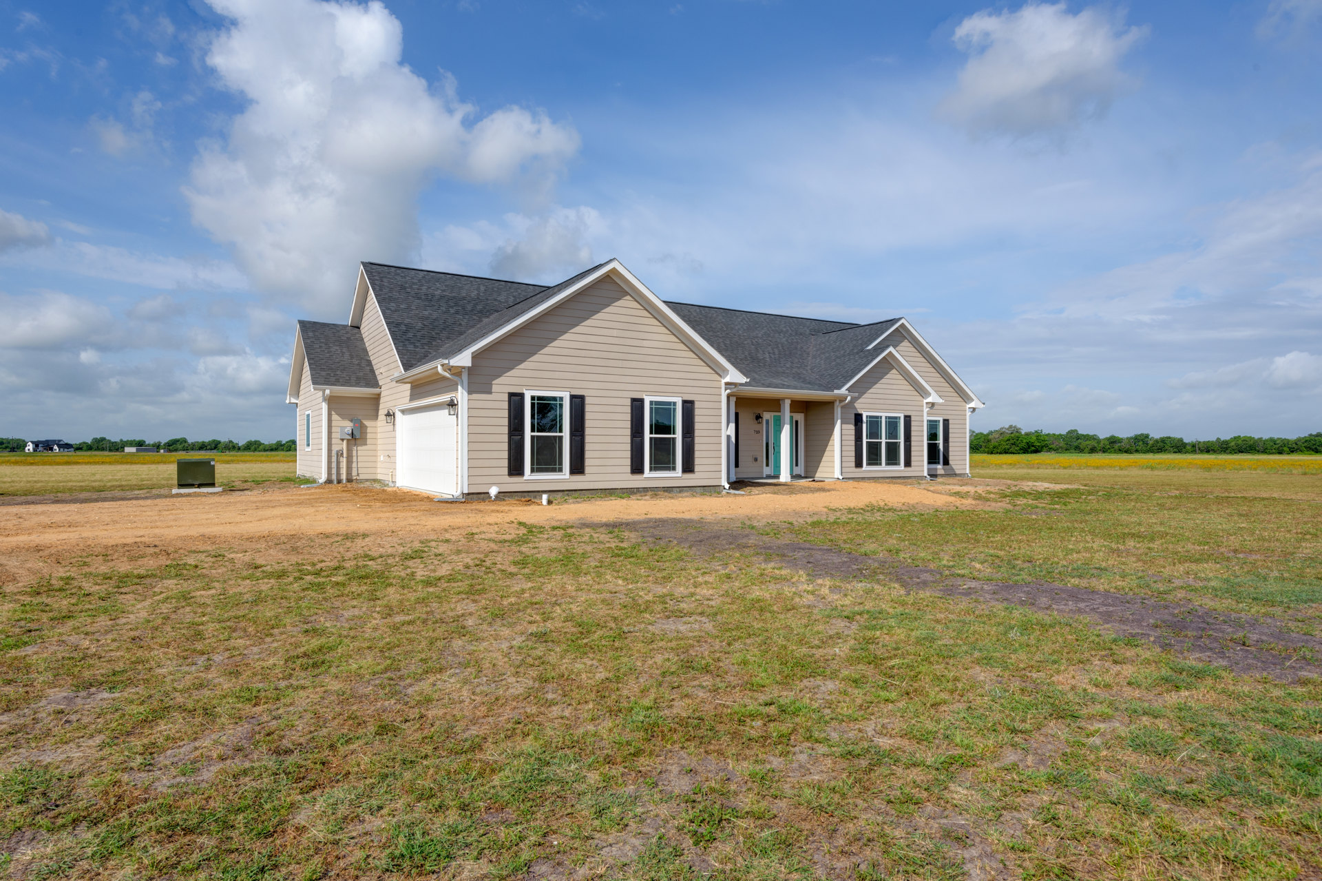 Two-story farmhouse with white roof, white-trimmed windows, and expansive green lawn under a partly cloudy sky