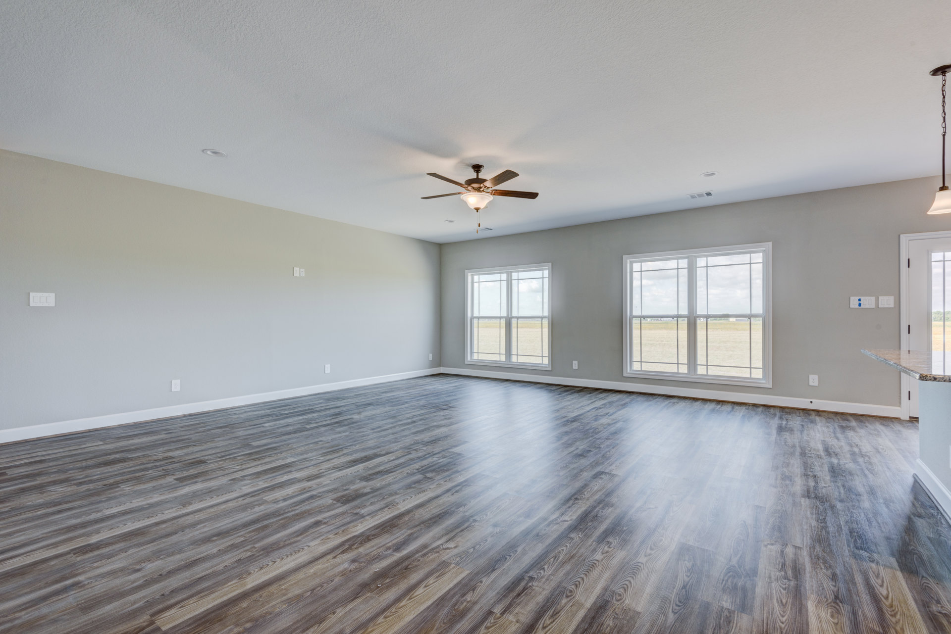 Wood flooring in a bright room with a ceiling fan, plaster ceiling, and large window overlooking a grassy field.